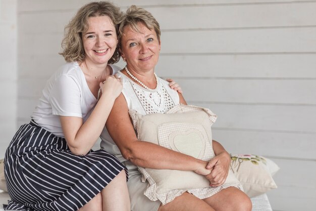 Reife lächelnde Mutter, die das Kissen sitzt mit ihrer schönen Tochter hält