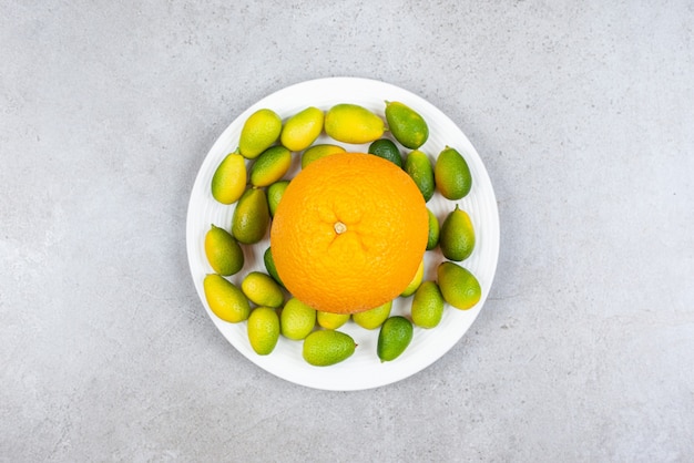 Reife Orange mit Haufen Kumquats auf weißem Teller.