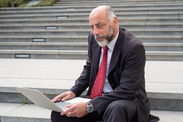 Reifer Geschäftsmann mit Laptop-Computer auf Straße