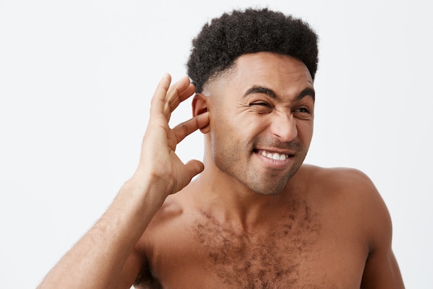 Reifer, gut aussehender schwarzhäutiger afrikanischer Mann mit lockigem Haar und nacktem Oberkörper, der versucht, am frühen Morgen nach dem Bad Wasser aus den Ohren zu holen. Mann macht sich bereit für die Arbeit.