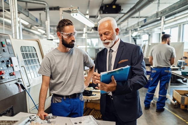 Reifer Ingenieur und junger Arbeiter, die zusammenarbeiten, während sie Papierkram in einer Industrieanlage erledigen