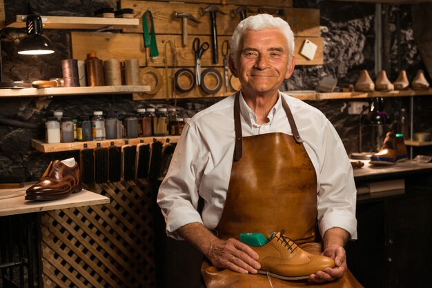 Reifer lächelnder Schuhmacher in der Werkstatt, die Schuhe hält