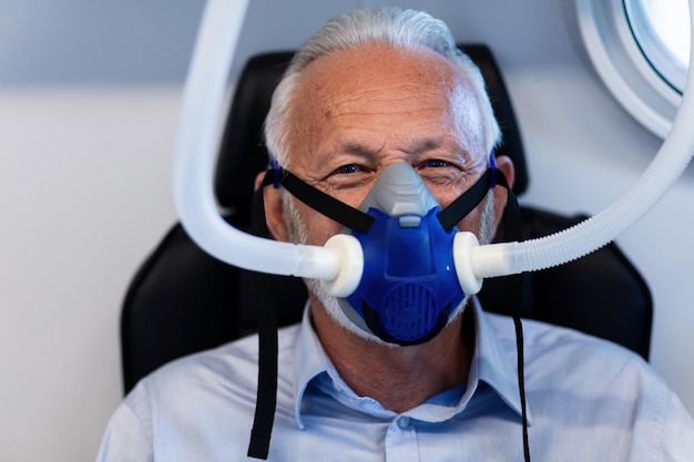 Reifer männlicher Patient, der während der hyperbaren Sauerstofftherapie eine Sauerstoffmaske trägt und in die Kamera schaut