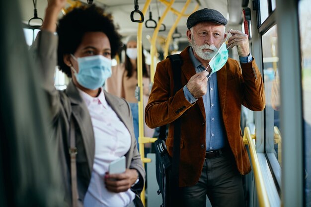 Reifer Mann, der in einem öffentlichen Verkehrsmittel eine schützende Gesichtsmaske aufsetzt