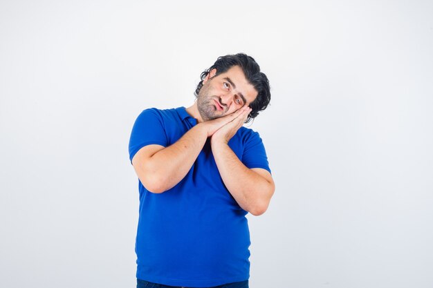 Reifer Mann, der sich auf Palmen als Kissen im blauen T-Shirt stützt und nachdenklich aussieht. Vorderansicht.