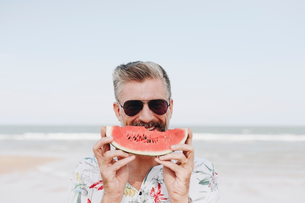 Kostenloses Foto reifer mann, der wassermelone am strand isst