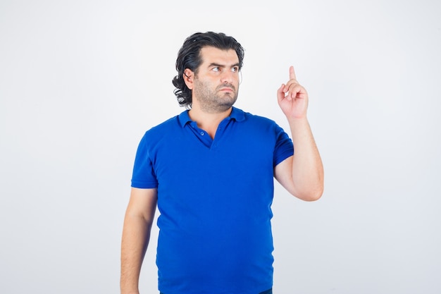 Reifer Mann, der Zeigefinger in der Eureka-Geste im blauen T-Shirt, in den Jeans und in der vernünftigen Vorderansicht anhebt.