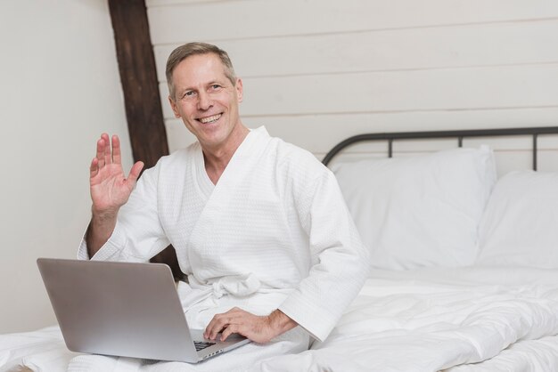 Reifer Mann des smiley, der einen Laptop im Bett mit Kopienraum hält