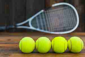 Kostenloses Foto reihe von grünen tennisbällen vor unscharfem schläger auf holztisch