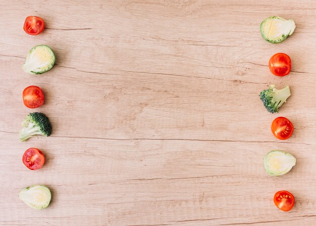 Reihe von halbierten Kirschtomaten; Rosenkohl; Brokkoli auf hölzernem Schreibtisch mit Kopienraum für das Schreiben des Textes