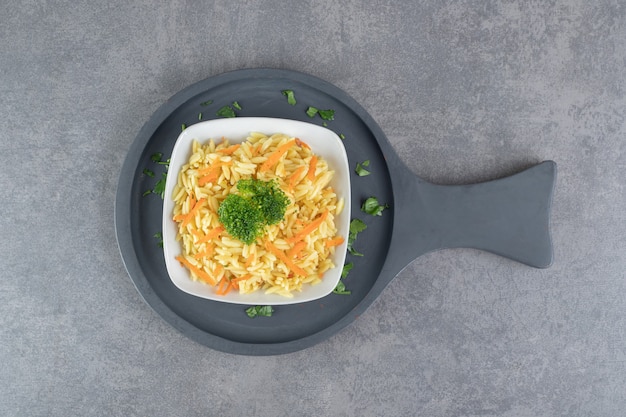 Reis mit Karottenscheiben und Brokkoli auf weißem Teller. Foto in hoher Qualität