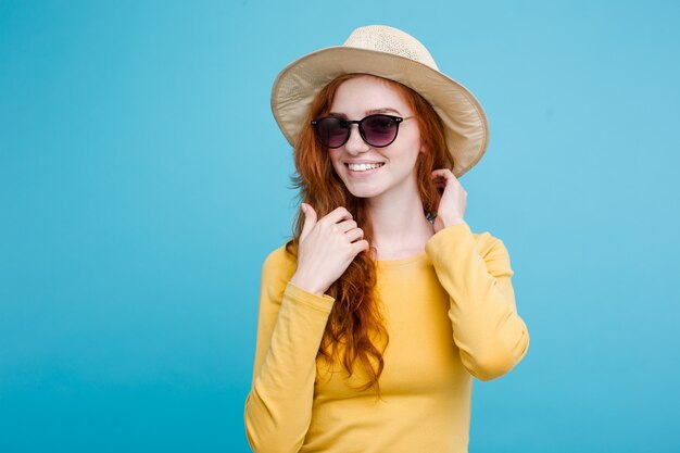 Reise-Konzept - Nahaufnahme Porträt junge schöne attraktive Redhair Mädchen mit trendy Hut und Sonnenbrille lächelnd. Blauer Pastellhintergrund. Platz kopieren