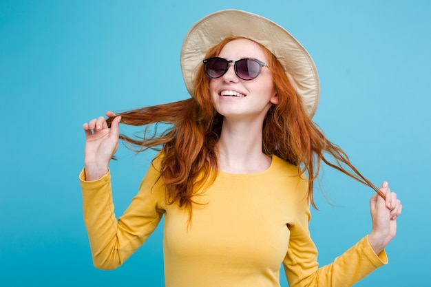 Reise-Konzept - Nahaufnahme Porträt junge schöne attraktive Redhair Mädchen mit trendy Hut und Sonnenbrille lächelnd. Blauer Pastellhintergrund. Platz kopieren