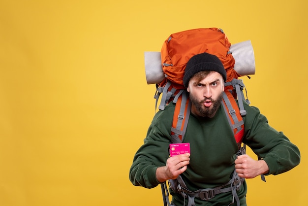 Reisekonzept mit ehrgeizigem jungen Mann mit Packpack und Bankkarte auf Gelb