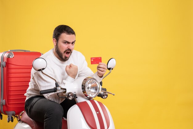 Reisekonzept mit einem jungen ehrgeizigen emotionalen reisenden Mann, der auf einem Motorrad mit einem Koffer darauf sitzt und eine Bankkarte auf Gelb hält
