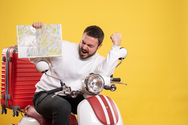 Reisekonzept mit glücklichem Kerl, der auf dem Motorrad mit Koffer darauf sitzt und Karte auf Gelb zeigt