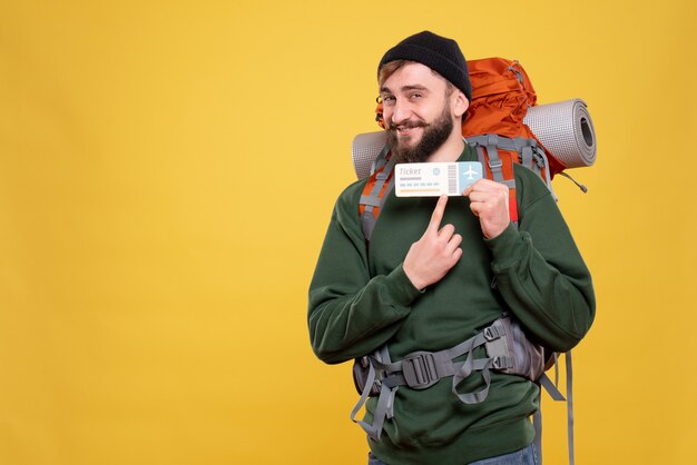 Reisekonzept mit lächelndem jungen Mann mit Packpack und Zeigeticket auf Gelb