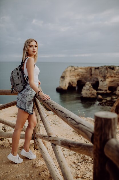 Reisende der jungen Schönheitblondine, die das Meer und die Klippe am schönen Portugal-Strand betrachtet.