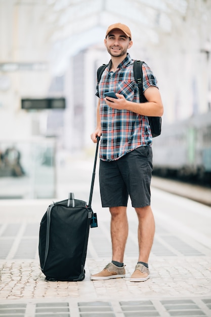 Reisender junger Mann mit Taschenblick im Telefon am Bahnhof