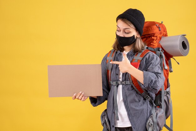 Reisendes Mädchen mit schwarzer Maske, die auf Pappe zeigt