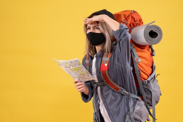 Reisendes Mädchen mit schwarzer Maske und Rucksack mit Karte und Blick auf etwas