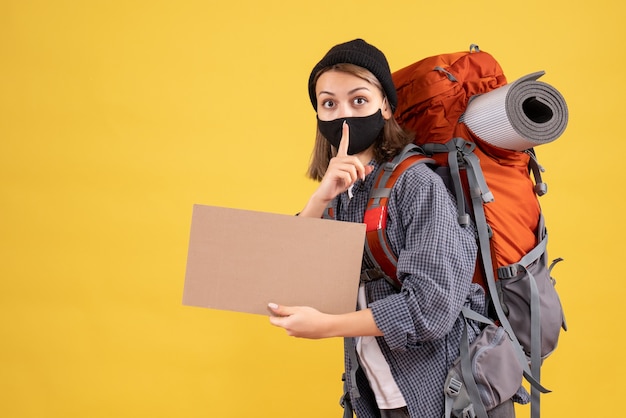 Reisendes Mädchen mit schwarzer Maske und Rucksack mit Pappe, die Stillezeichen macht