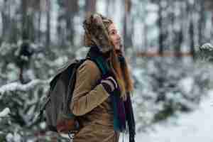 Kostenloses Foto reisendmädchen in der warmen winterjacke mit der pelzhaube und großem rucksack gehend in wald