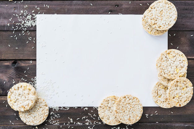 Reiskörner und luftgestoßener Reiskuchen auf weißem leerem Papier über dem hölzernen Schreibtisch