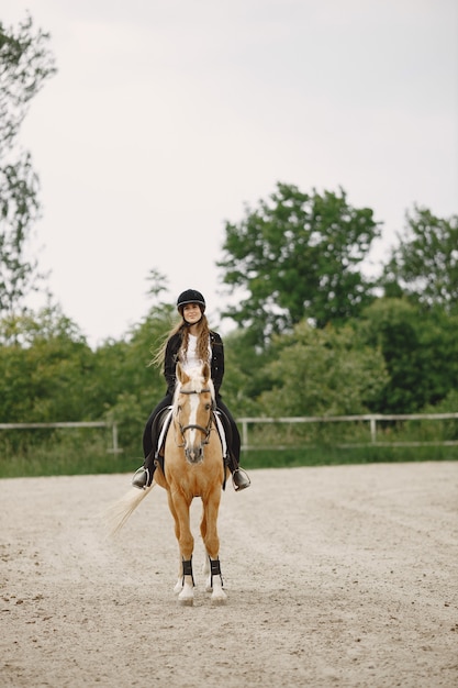 Reiterfrau, die ihr Pferd auf einer Ranch reitet. Frau hat langes Haar und schwarze Kleidung. Reiterin auf ihrem braunen Pferd.