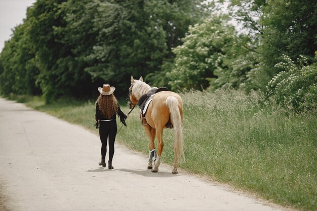 Reiterfrau, die mit ihrem Pferd auf einer Ranch geht. Frau hat langes Haar und schwarze Kleidung. Weiblicher Reiter, der ein Pferd hält Zügel.