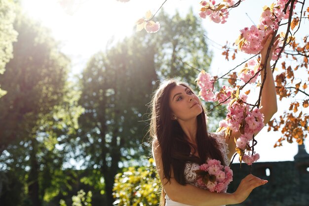 Reizend junge Frau im rosa Kleid wirft vor einem Kirschblüte-Baum voll von den rosa Blumen auf