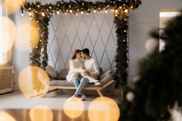 Reizend junge Paare in der gemütlichen weißen Hauptkleidung wirft in einem Raum mit Weihnachtsbaum auf