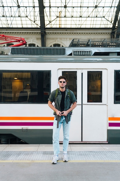 Kostenloses Foto reizend junger reisender, der den bügel des rucksacks stehend auf plattform justiert