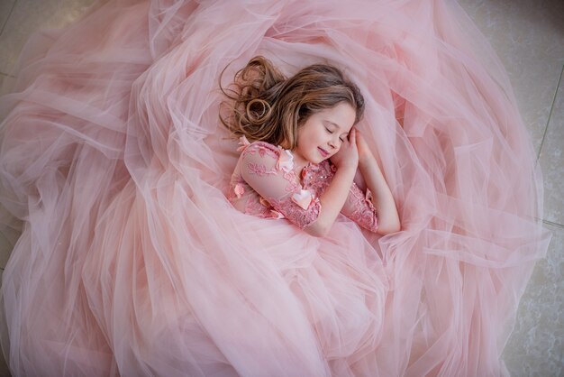 Reizend kleines Mädchen im rosa Kleid schaut reizend, während sie auf dem Fußboden schläft