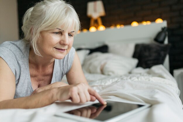 Reizende Frau, die Tablette auf Bett verwendet