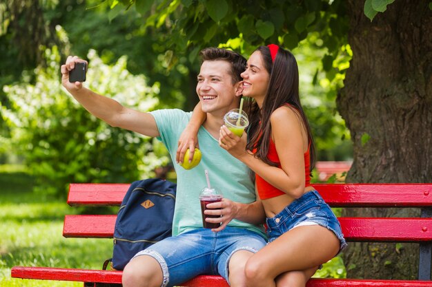 Reizende junge Paare, die das gesunde Lebensmittel nimmt Selbstporträt im Park halten