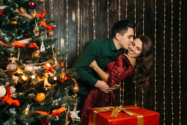 Reizende Paare in der Liebe, die nahe Weihnachtsbaum umfasst