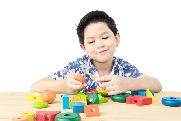 Reizender asiatischer Junge ist buntes hölzernes Blockspielzeug des Spiels