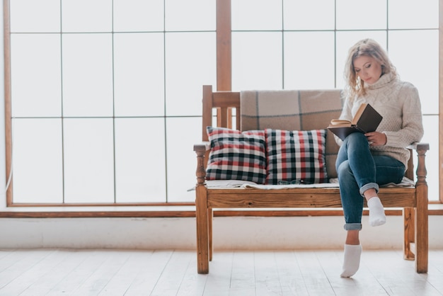 Kostenloses Foto reizendes frauenlesebuch auf couch nahe fenster