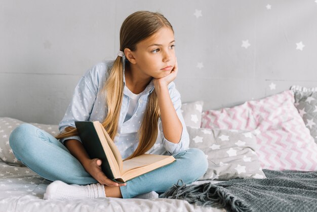 Reizendes glückliches Mädchen, das mit einem Buch aufwirft