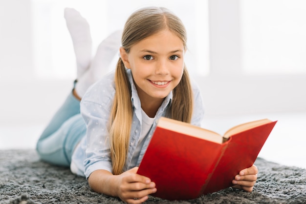 Reizendes glückliches Mädchen, das mit einem Buch aufwirft