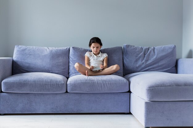 Reizendes kleines Mädchen mit Smartphone auf dem Sofa