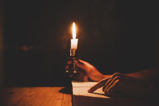 Religiöse Mannholding beleuchtete Kerzen und Lesen der heiligen Bibel und Beten in der Kirche