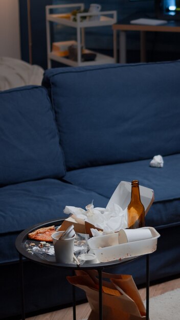 Reste von pizza leeren bierflaschen und servietten auf dem tisch im unordentlichen wohnzimmer