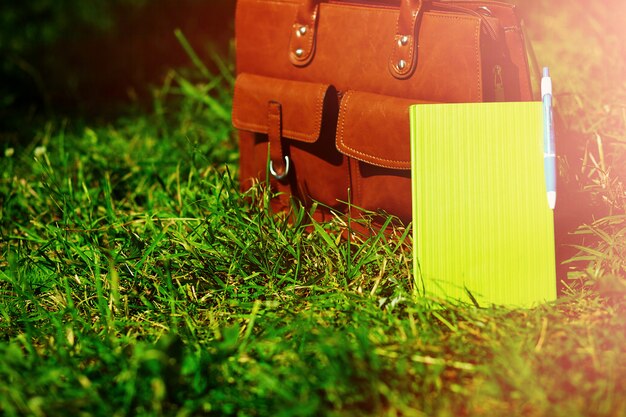 Retro braune Mann Ledertasche und Notizbuch im hellen bunten Sommergras im Park