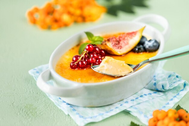 Rezept für Crème Brûlée Dessert mit frischen Feigen Blaubeeren und Johannisbeeren auf einem grünen Steintisch in Herbstkomposition