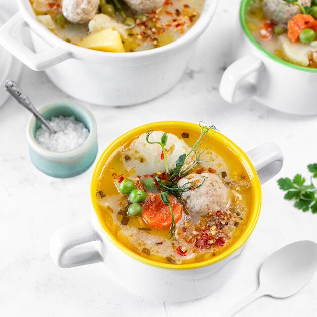 Rezept für Suppe mit Fleischbällchen Blumenkohl Baby Erbsen Karotten und Sahne auf weißem Hintergrund Square