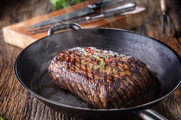 Rindersteak. saftiges rib-eye-steak in pfanne auf holzbrett mit kräutern und pfeffer.