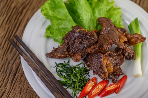 Rindfleisch gebratenes thailändisches Essen auf einem weißen Teller mit Frühlingszwiebeln, Kaffirlimettenblättern, Chilis, Essstäbchen, Salat und Chilipaste in einer Tasse.