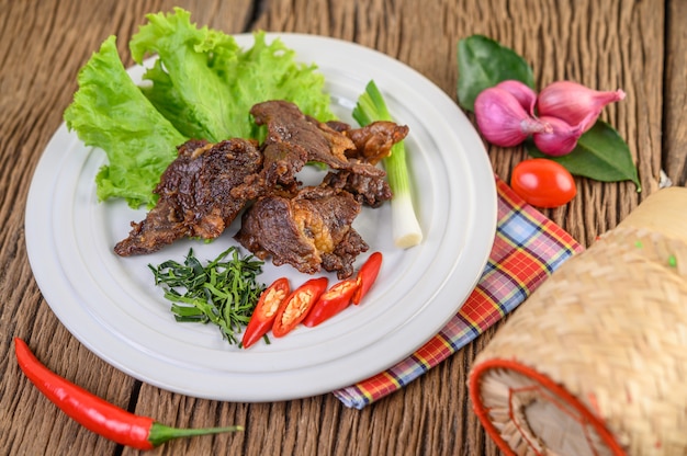 Rindfleisch gebratenes thailändisches Essen auf einem weißen Teller mit Frühlingszwiebeln, Kaffirlimettenblättern, Chilis, Salat, roten Zwiebeln und Tomaten.